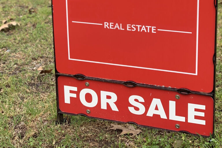 A red real estate for sale sign on land