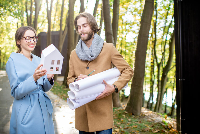 A couple with a model home and wraps of paper outdoors